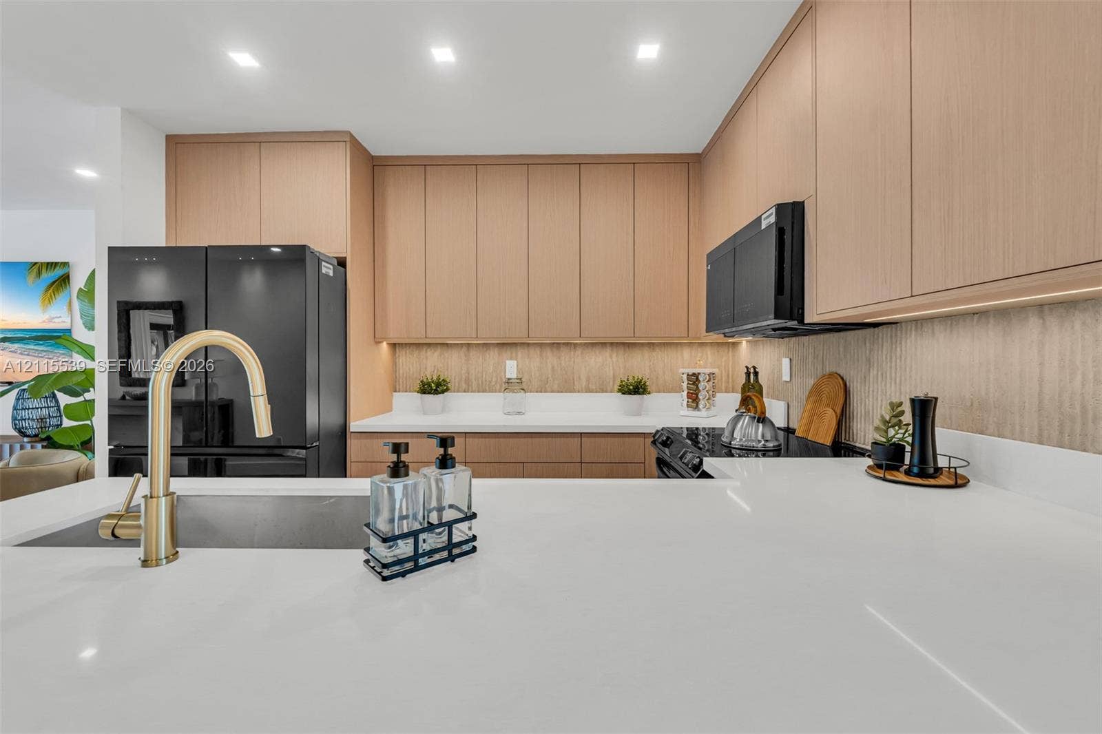 381 SE 6th Terrace, Pompano Beach, FL 33060 Kitchen featuring flat-panel wood-finish cabinetry, white solid-surface countertops, black integrated appliances, and a brass-tone gooseneck faucet