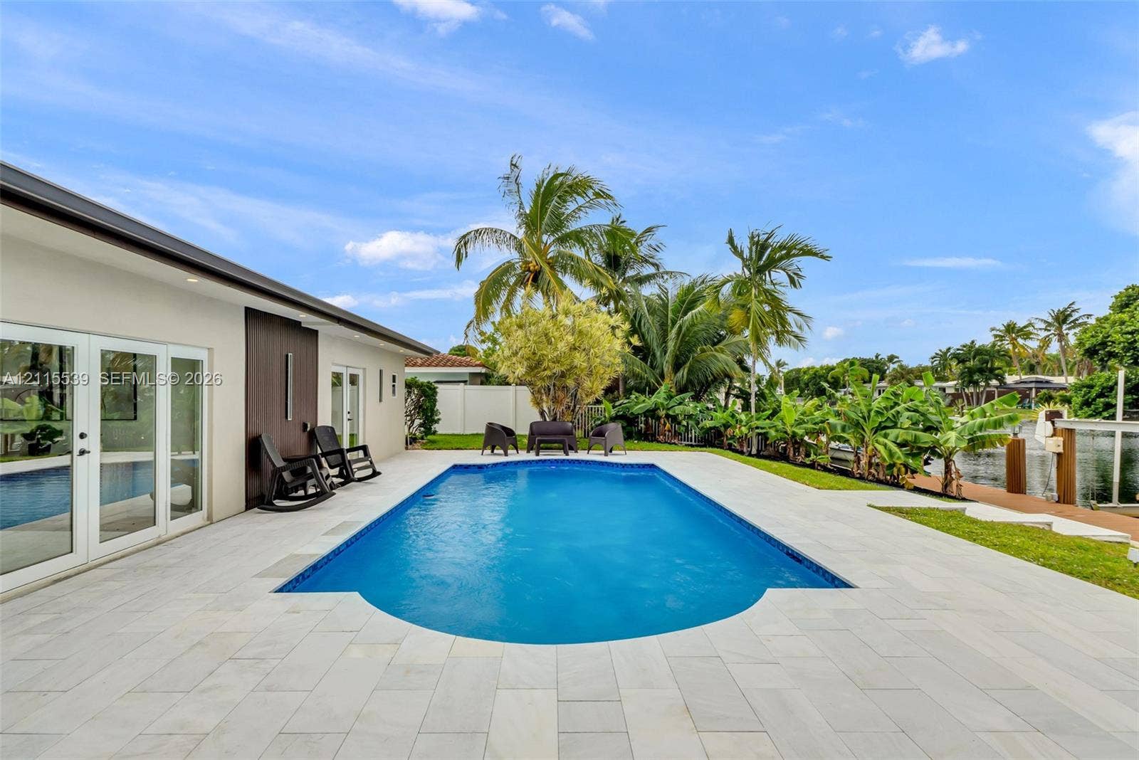 381 SE 6th Terrace, Pompano Beach, FL 33060 In-ground swimming pool with stone-tile decking, waterfront bulkhead, and mature tropical landscaping