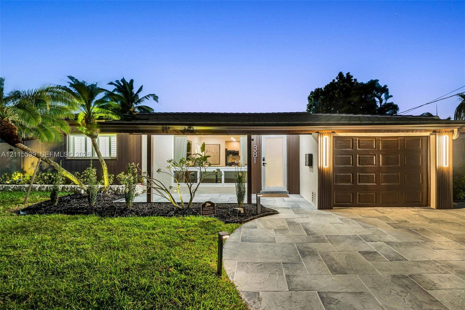 381 SE 6th Terrace, Pompano Beach, FL 33060 Single-story exterior featuring a natural stone-patterned paved driveway, integrated vertical exterior wall lighting, and landscaped front lawn with mature palm trees