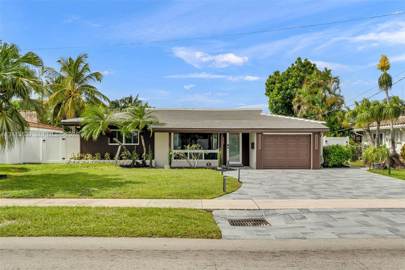381 SE 6th Terrace, Pompano Beach, FL 33060 Single-story residence featuring a multi-toned exterior, a natural stone paved driveway, an attached garage, and mature palm landscaping