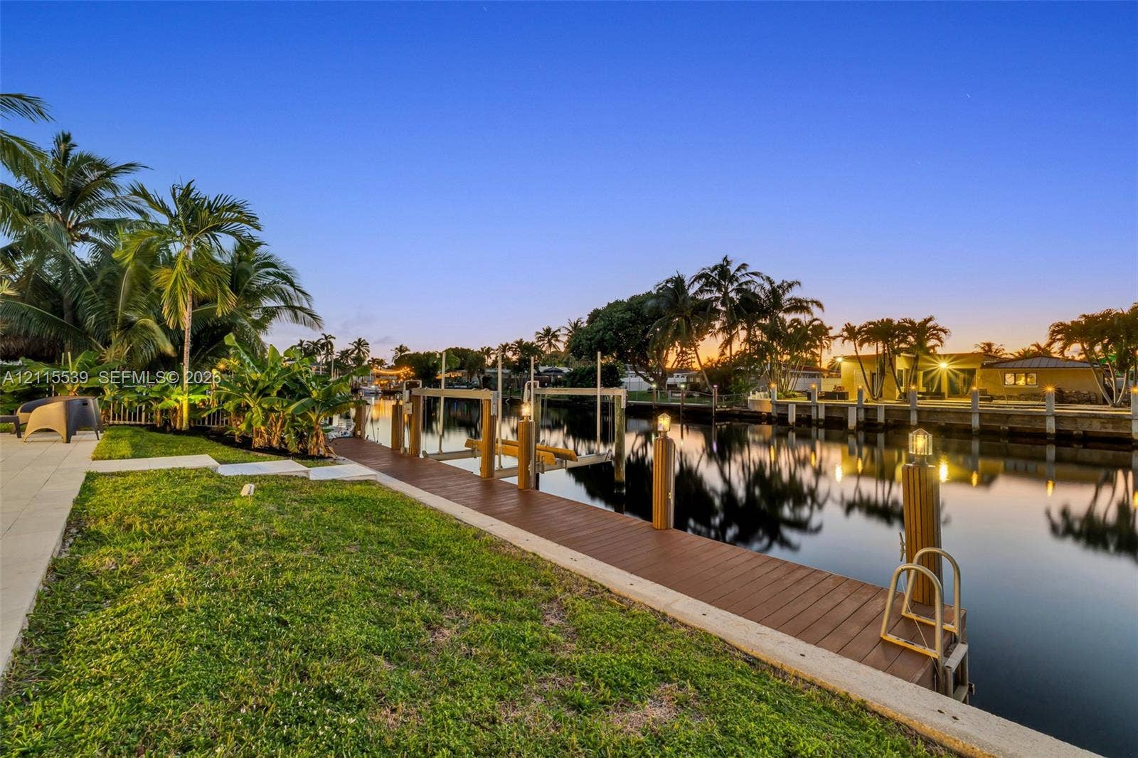 381 SE 6th Terrace, Pompano Beach, FL 33060 Waterfront property featuring a private wooden dock, boat lift, concrete seawall, and landscaped lawn with mature palm trees