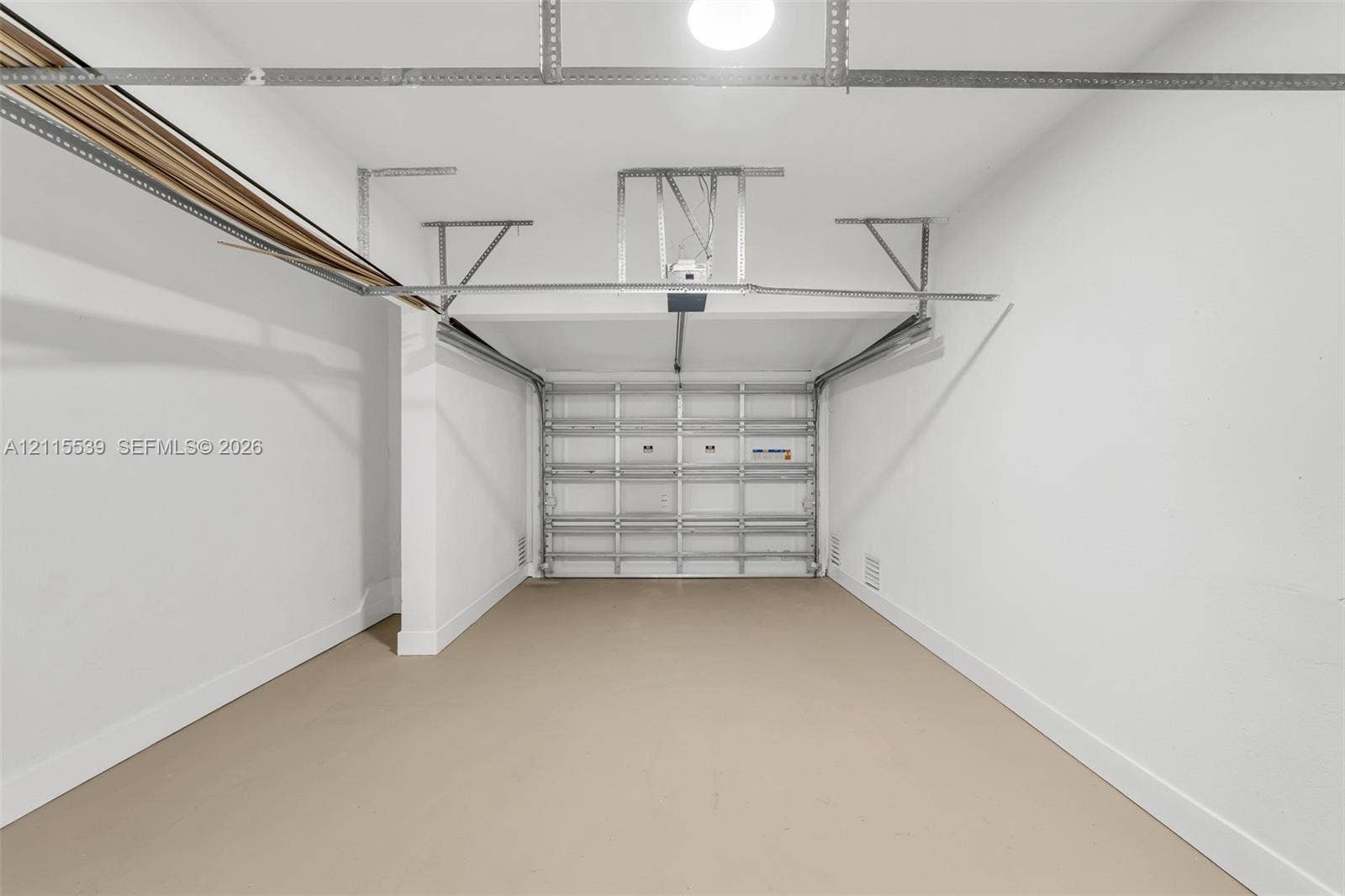 381 SE 6th Terrace, Pompano Beach, FL 33060 Enclosed garage featuring finished concrete flooring, painted walls, an automated sectional door, and overhead lighting