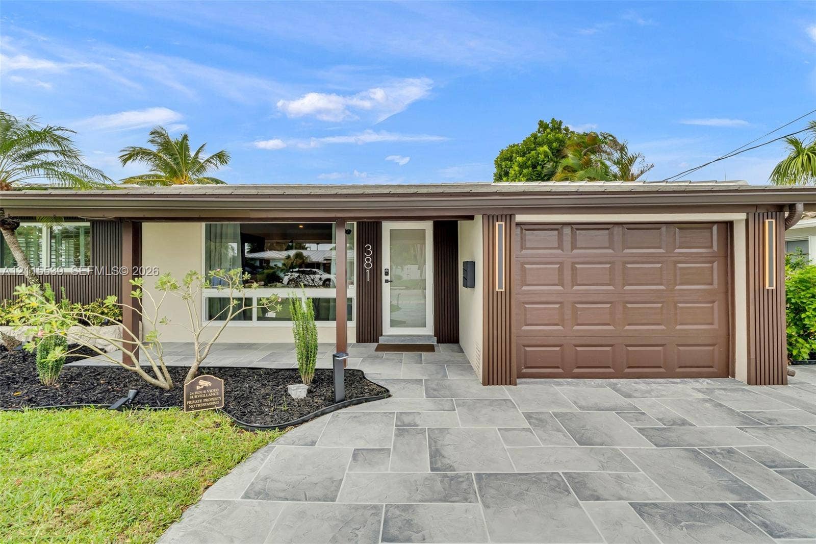 381 SE 6th Terrace, Pompano Beach, FL 33060 Single-story exterior featuring a stone-paver driveway, integrated garage with a paneled door, covered front entryway, and vertical wood-slat accent siding
