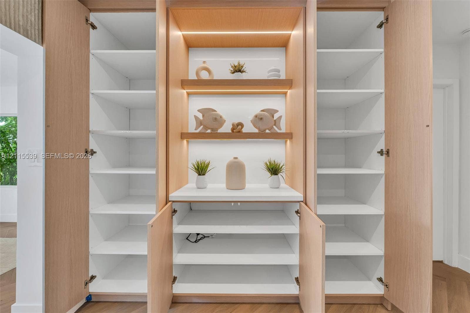 381 SE 6th Terrace, Pompano Beach, FL 33060 Custom built-in cabinetry featuring light wood-finish veneer, integrated LED shelf lighting, fixed white shelving, and a central solid-surface countertop