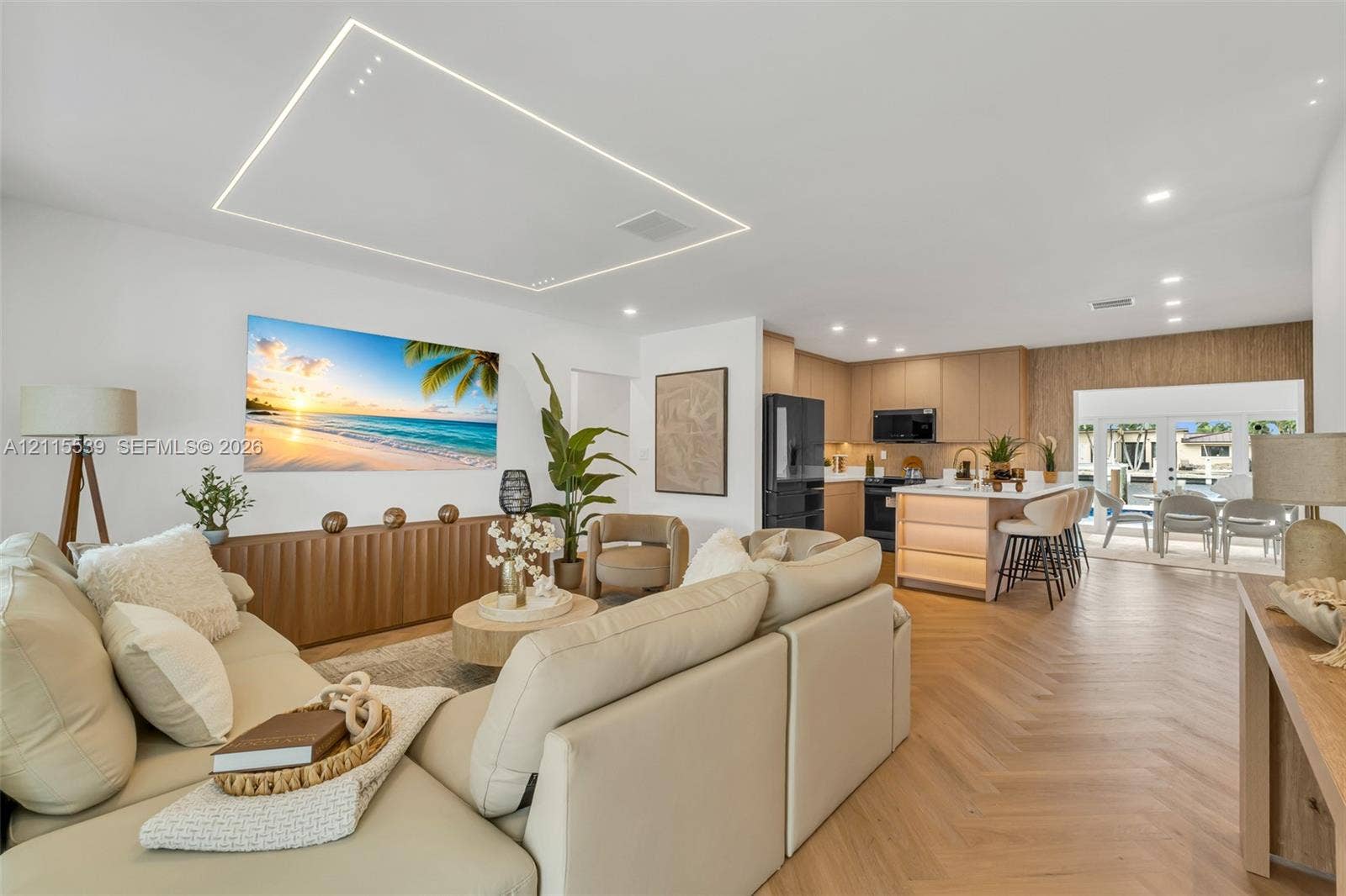 381 SE 6th Terrace, Pompano Beach, FL 33060 Open-concept living space featuring wood-finish flooring in a herringbone pattern, a recessed rectangular tray ceiling with perimeter lighting, recessed ceiling spotlights, a kitchen island with integrated under-counter lighting, and French doors