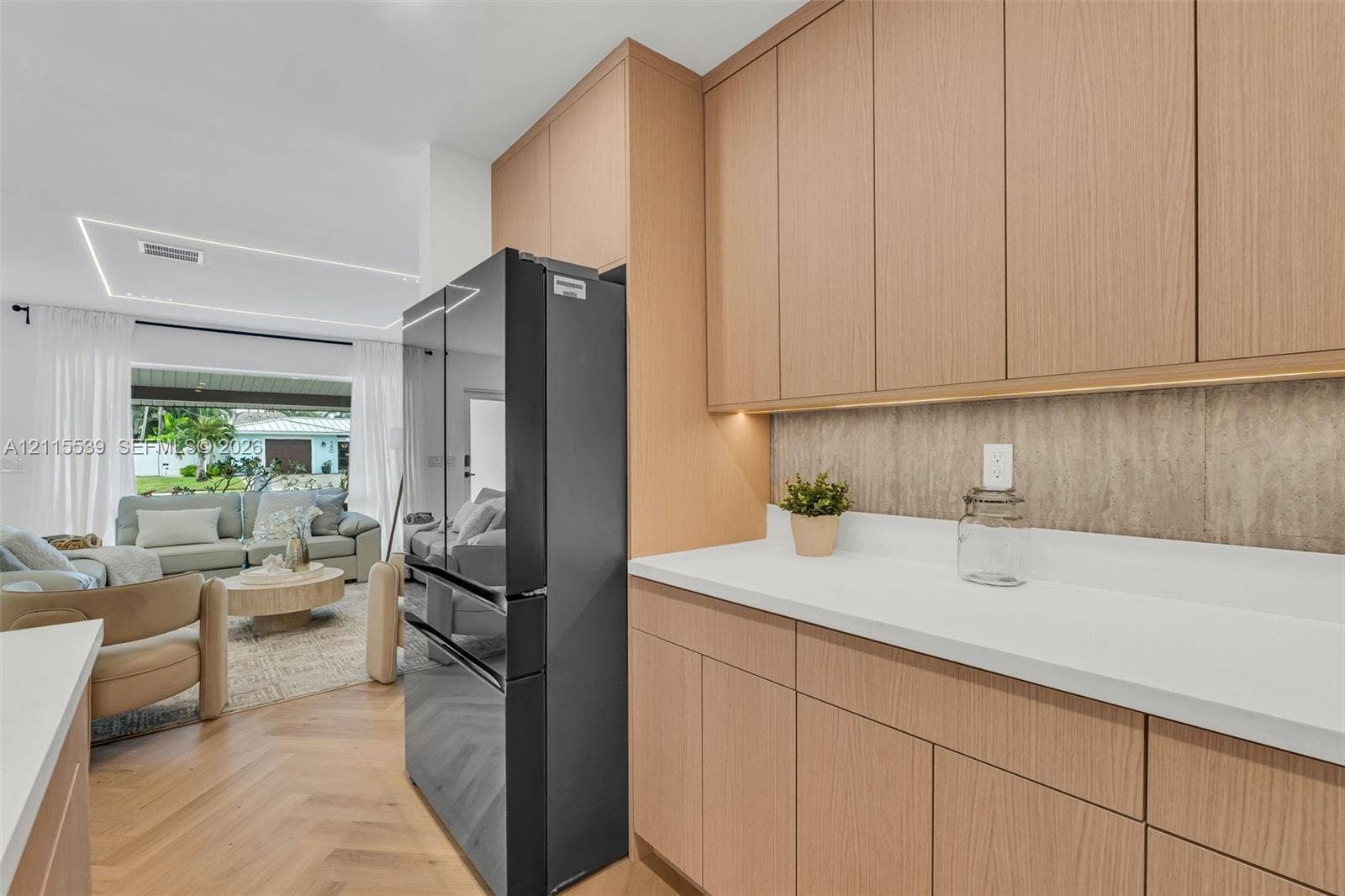 381 SE 6th Terrace, Pompano Beach, FL 33060 Flat-panel light wood cabinetry featuring under-cabinet lighting, solid surface countertops, textured backsplash, and herringbone-pattern wood-finish flooring