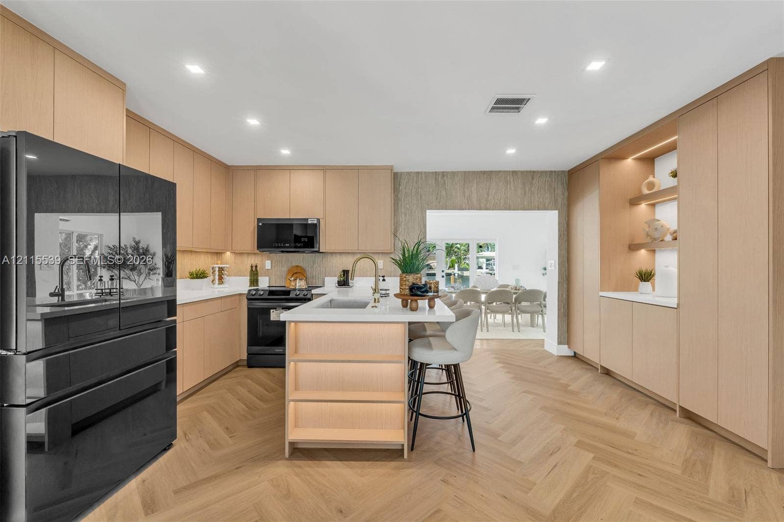 381 SE 6th Terrace, Pompano Beach, FL 33060 Kitchen featuring light wood-finish cabinetry, herringbone-patterned wood flooring, a central island with an integrated sink and under-counter lighting, and built-in floor-to-ceiling storage