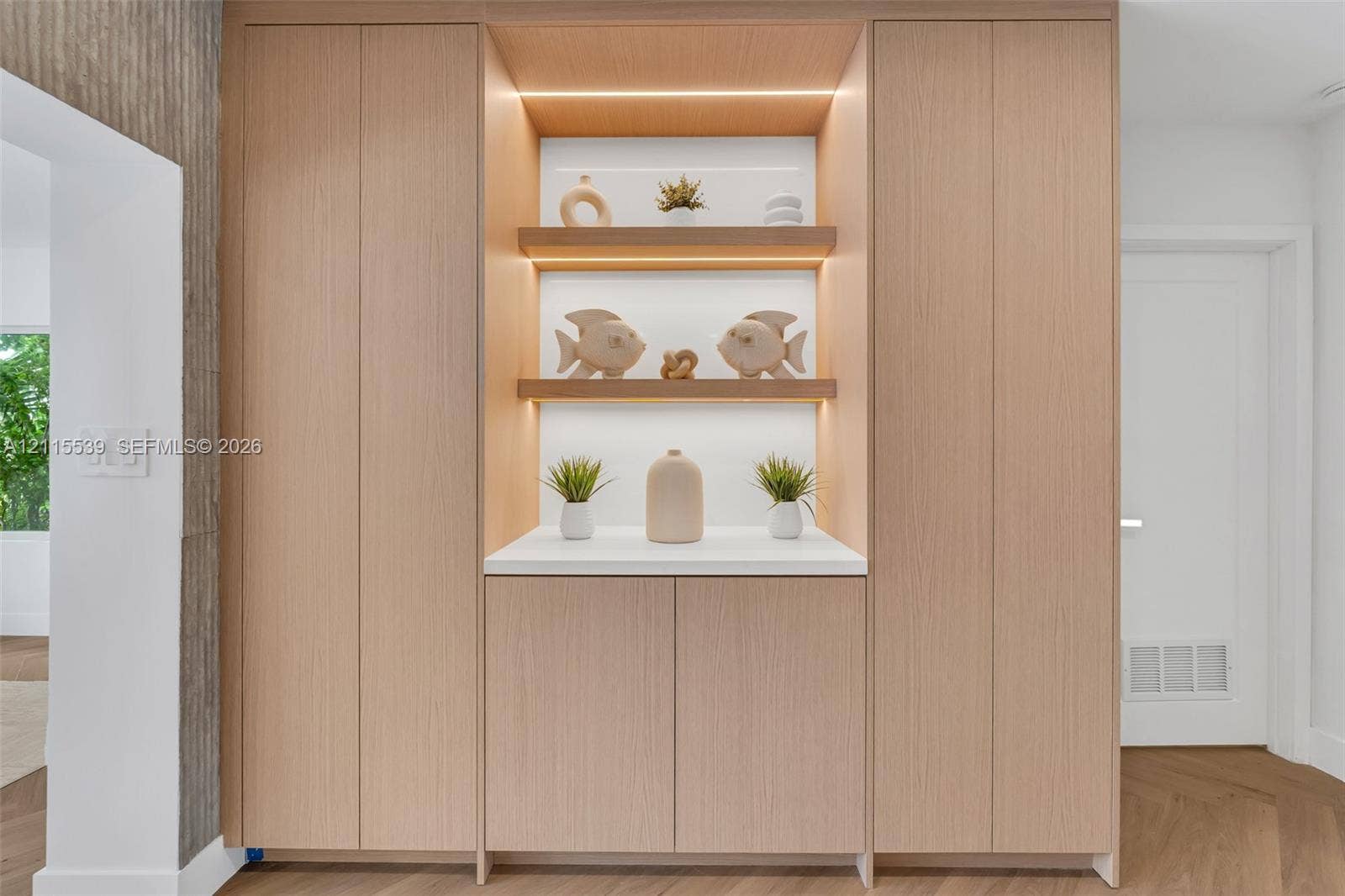 381 SE 6th Terrace, Pompano Beach, FL 33060 Floor-to-ceiling cabinetry with light wood-finish veneer, integrated recessed display shelving, built-in task lighting, white solid-surface countertop, and herringbone wood-finish flooring
