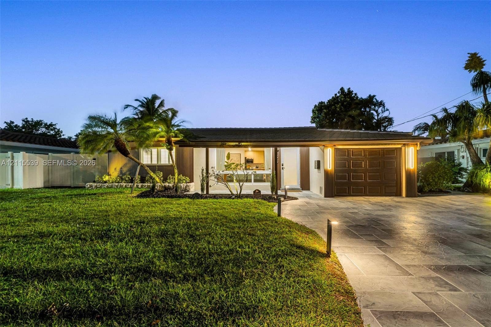 381 SE 6th Terrace, Pompano Beach, FL 33060 Single-story residence featuring a paved driveway, integrated garage with sectional door, low-pitched roof, manicured lawn, and professional exterior landscape lighting