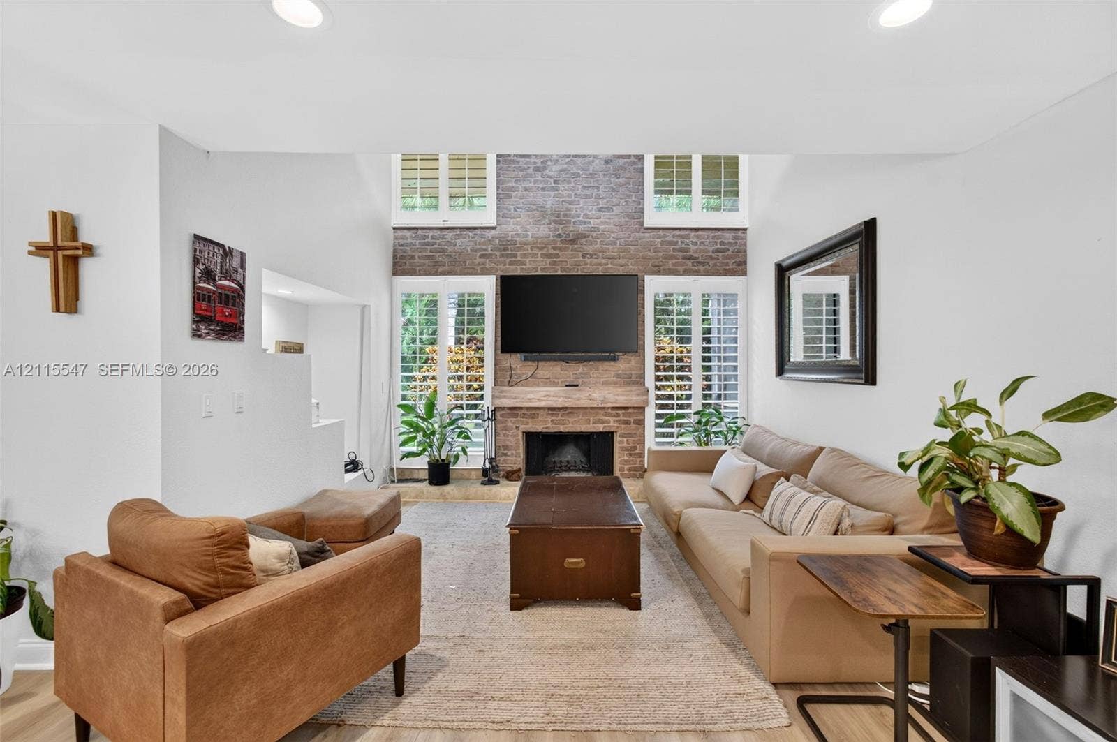 22862 Ironwedge Drive, #0, Boca Raton, FL 33433 Double-height living room featuring a floor-to-ceiling brick fireplace, recessed lighting, and plantation shutters flanking multi-pane glass doors