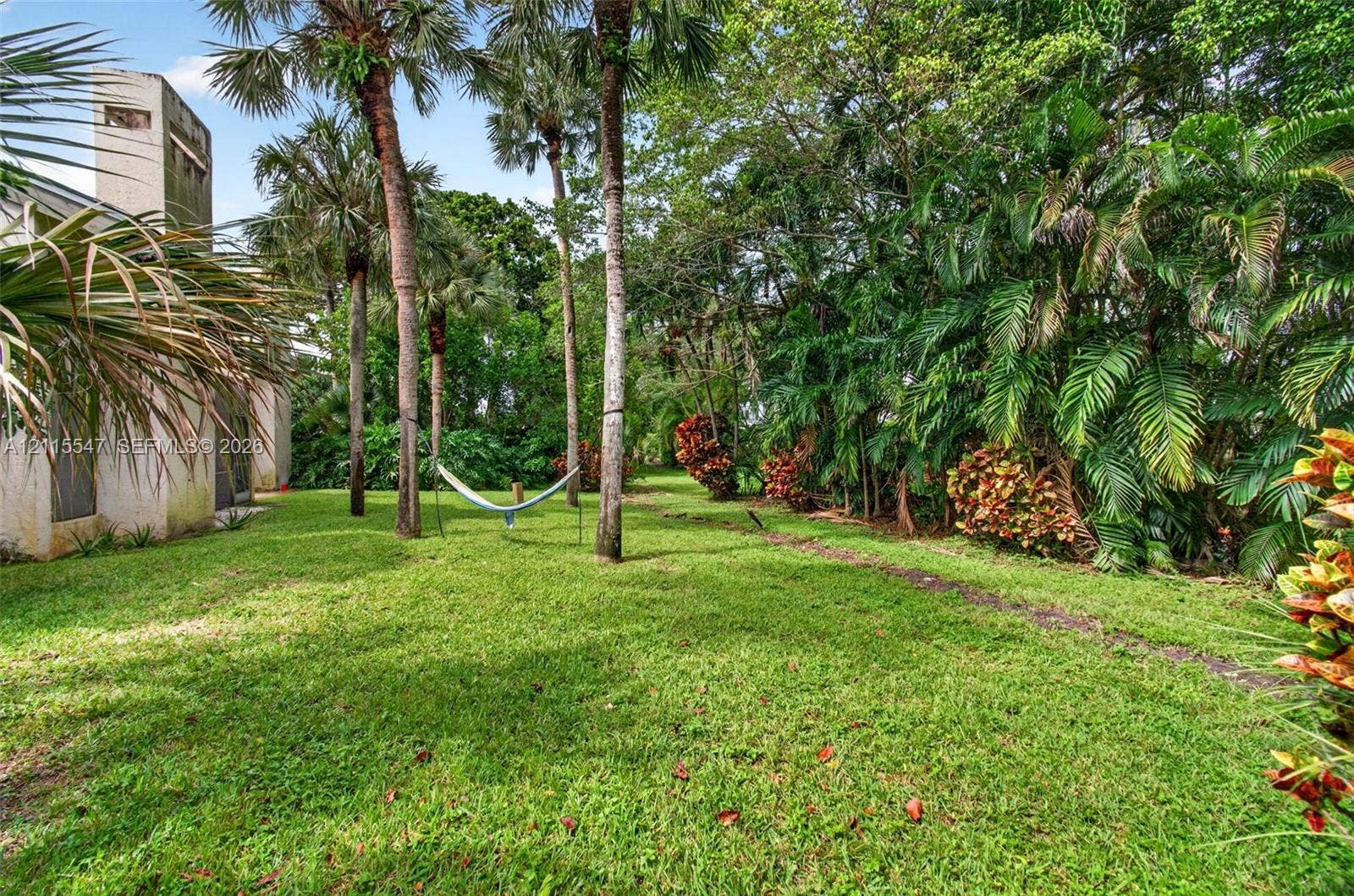 22862 Ironwedge Drive, #0, Boca Raton, FL 33433 Expansive lawn area featuring mature palm trees, dense tropical foliage, and a textured stucco exterior chimney