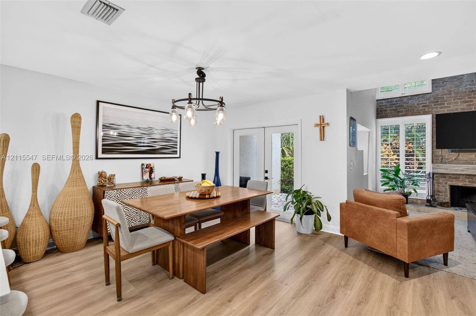 22862 Ironwedge Drive, #0, Boca Raton, FL 33433 Open-concept room featuring wood-finish flooring, a multi-arm iron chandelier, double glass-paneled exterior doors, and a floor-to-ceiling decorative brick fireplace with a wood mantel