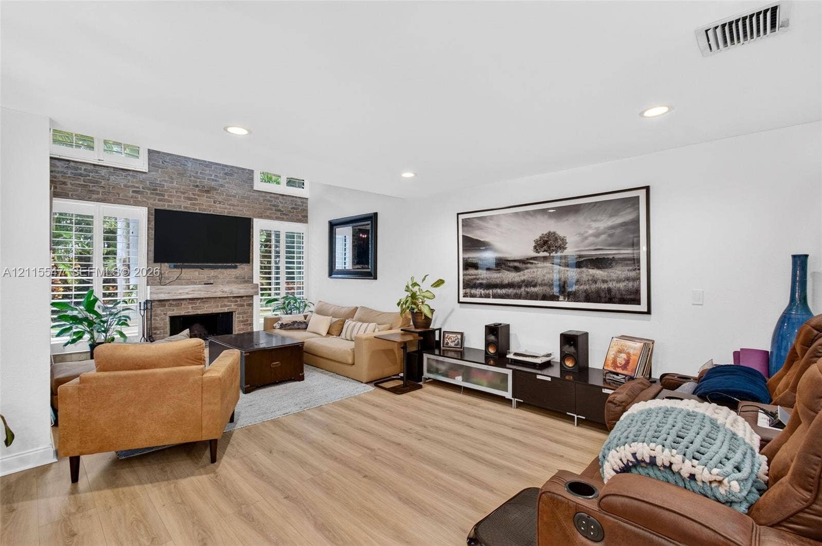 22862 Ironwedge Drive, #0, Boca Raton, FL 33433 Living area featuring wood-finish flooring, floor-to-ceiling brick fireplace surround, natural wood mantel, and white plantation shutters