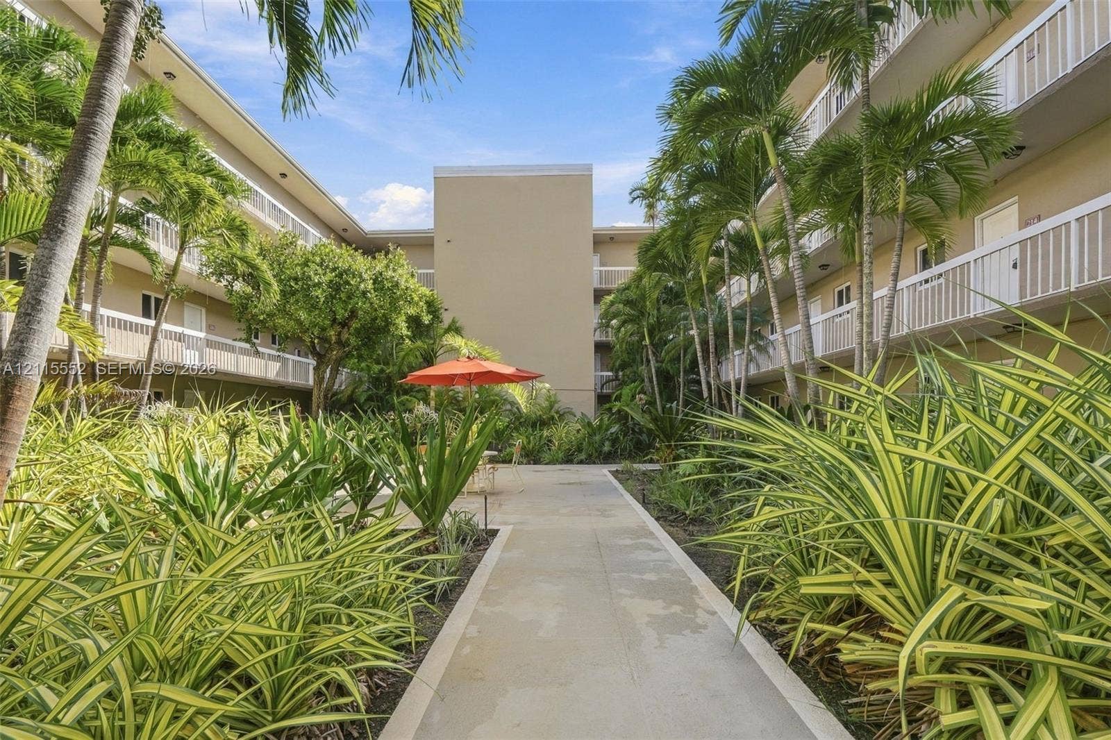 7805 Camino Real, #H-220, Miami, FL 33143 Central courtyard featuring concrete walkways, mature palm trees, tiered exterior balconies with white railings, and native tropical landscaping