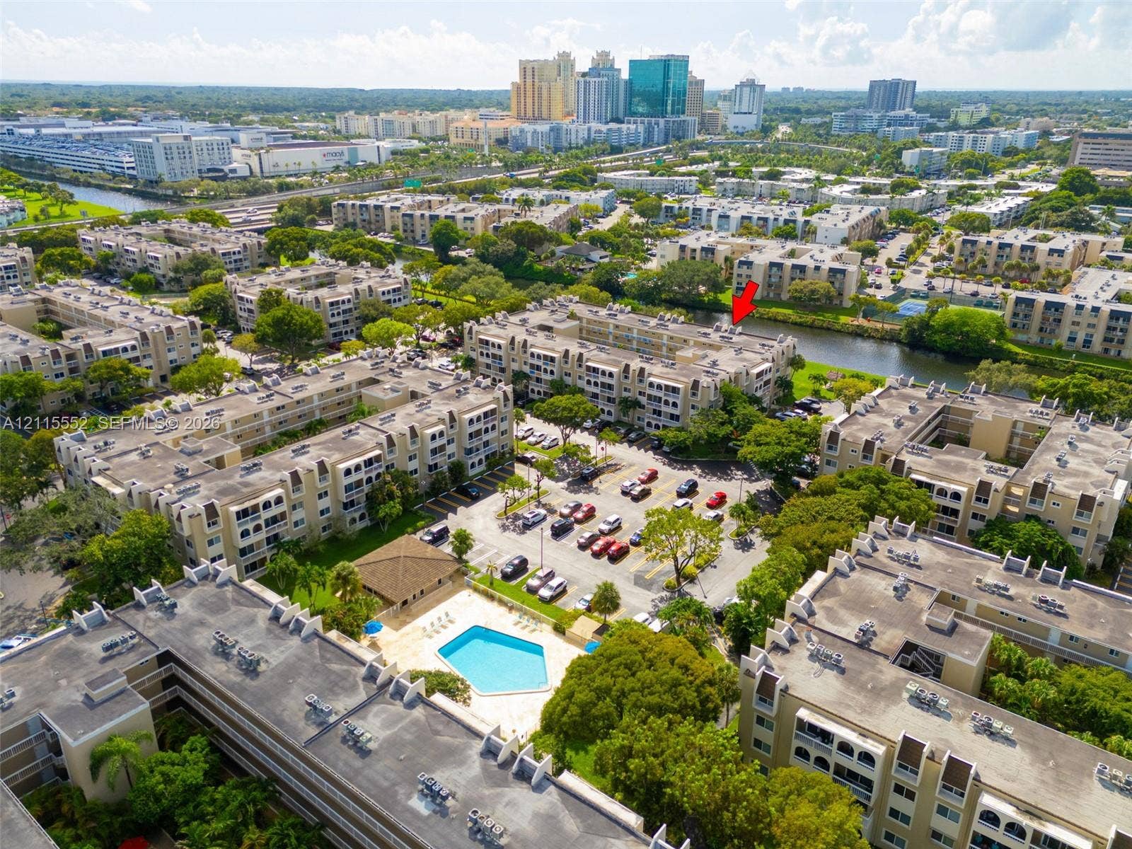 7805 Camino Real, #H-220, Miami, FL 33143 Aerial perspective of a multi-story residential complex featuring an outdoor swimming pool, paved surface parking, and waterfront grounds