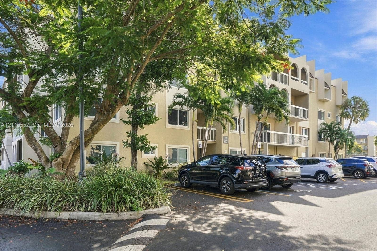 7805 Camino Real, #H-220, Miami, FL 33143 Multi-story building exterior featuring stucco siding, arched architectural detailing, private railed balconies, and surface parking