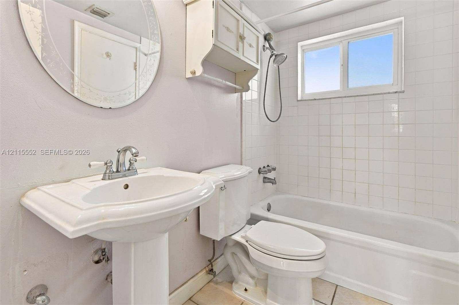 7805 Camino Real, #H-220, Miami, FL 33143 Pedestal sink with chrome dual-handle faucet, oval mirror, wall-mounted storage cabinet, and white tile-surround bathtub featuring a handheld showerhead