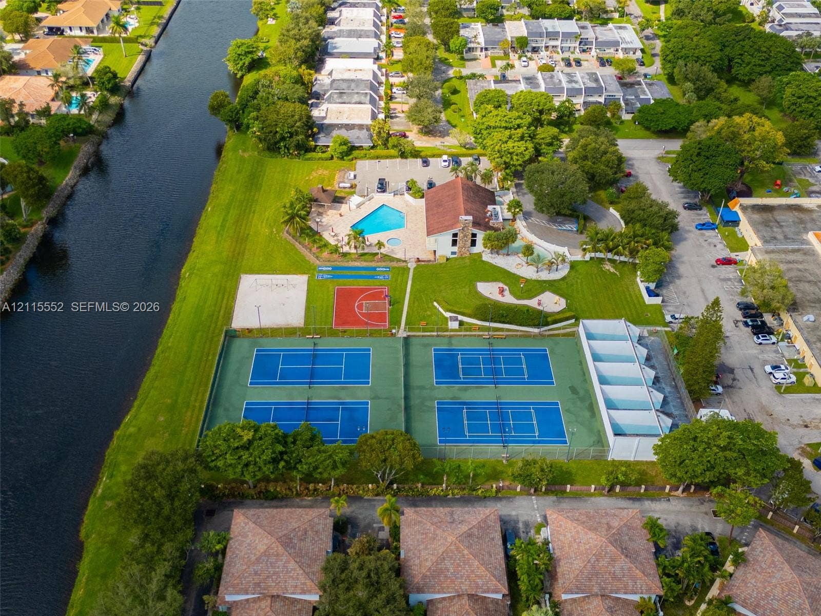 7805 Camino Real, #H-220, Miami, FL 33143 Aerial perspective featuring waterfront grounds, four tennis courts, an outdoor swimming pool, a basketball court, and a sand volleyball court