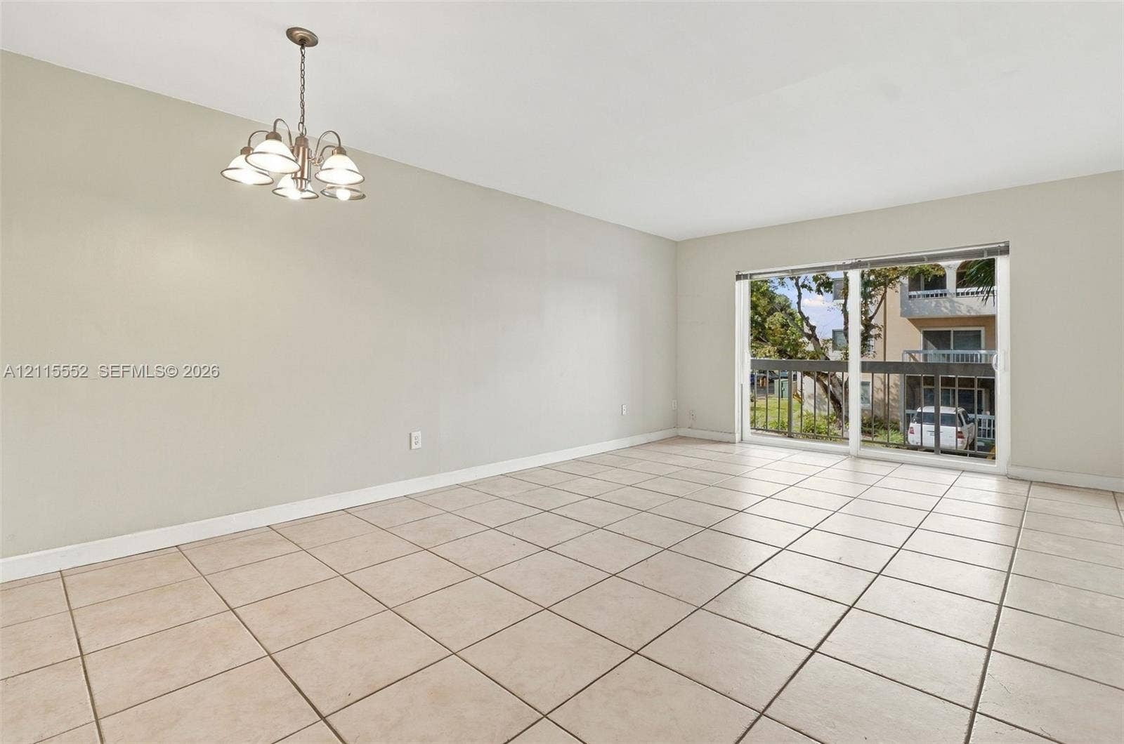 7805 Camino Real, #H-220, Miami, FL 33143 Neutral-tone interior space featuring ceramic tile flooring, a multi-light chandelier, and large sliding glass doors providing access to a private balcony with metal railing