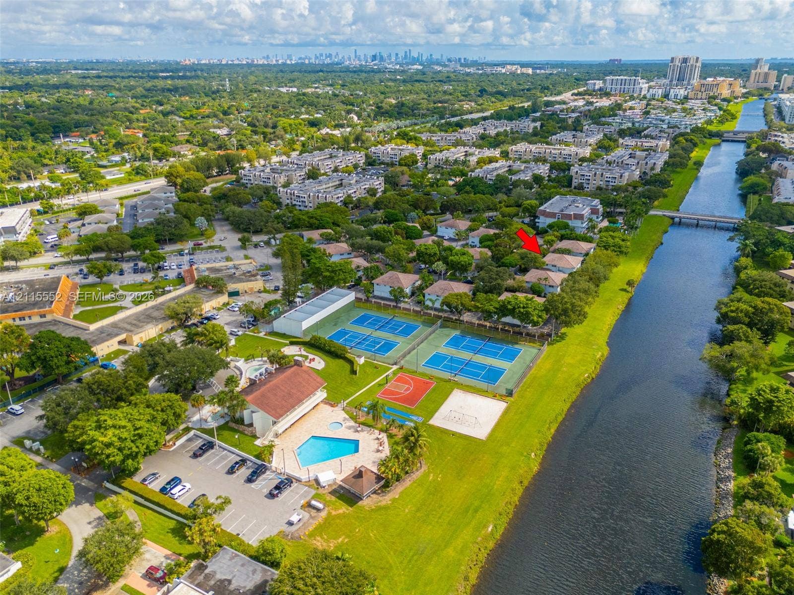 7805 Camino Real, #H-220, Miami, FL 33143 Aerial perspective of communal amenities featuring two tennis courts, a basketball court, a swimming pool, and a canal-side walking path