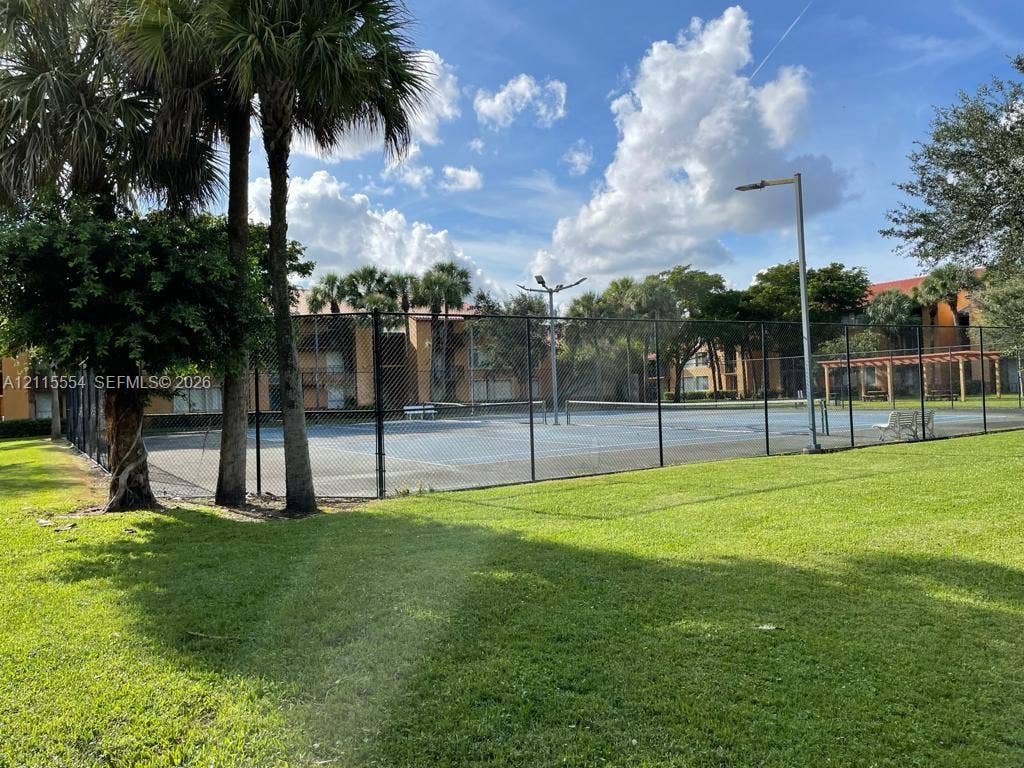 10781 Cleary Boulevard, #210, Plantation, Plantation, FL 33324 Fenced tennis court with overhead lighting, manicured green space, and mature palm trees