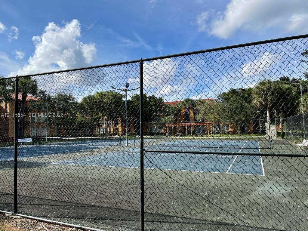 10781 Cleary Boulevard, #210, Plantation, Plantation, FL 33324 Tennis court with a blue surface, chain-link perimeter fencing, and pole-mounted lighting