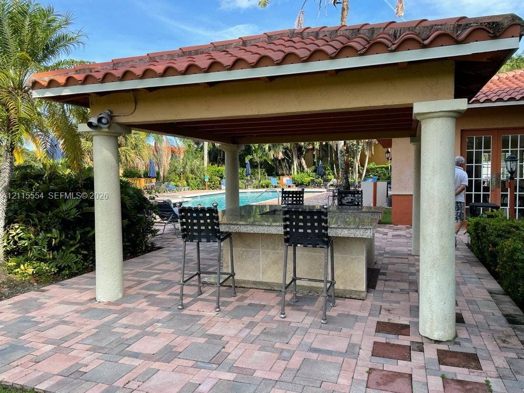 10781 Cleary Boulevard, #210, Plantation, Plantation, FL 33324 Covered outdoor kitchen featuring a stone-topped island, paver patio flooring, and classical columns under a terracotta-tiled roof