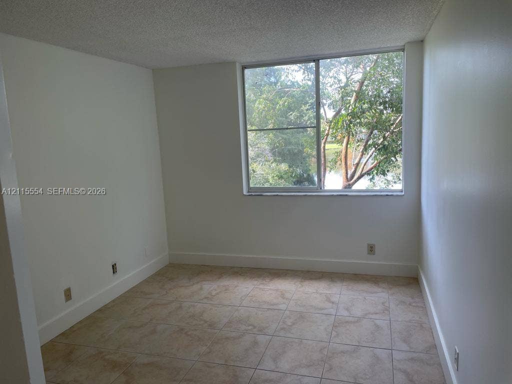10781 Cleary Boulevard, #210, Plantation, Plantation, FL 33324 Neutral-toned interior featuring oversized tile flooring, a sliding glass window, and water-front scenery with mature trees