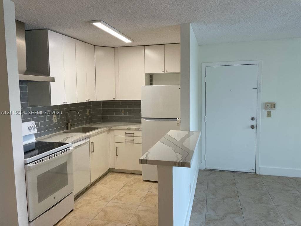 10781 Cleary Boulevard, #210, Plantation, Plantation, FL 33324 Kitchen featuring white cabinetry, quartz countertops with a waterfall edge, subway tile backsplash, stainless steel range hood, and tile flooring