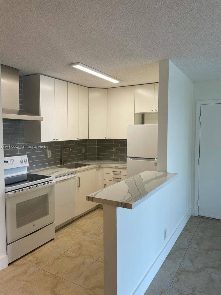 10781 Cleary Boulevard, #210, Plantation, Plantation, FL 33324 Kitchen featuring white flat-panel cabinetry, a stone-patterned breakfast bar, gray subway tile backsplash, and tile flooring