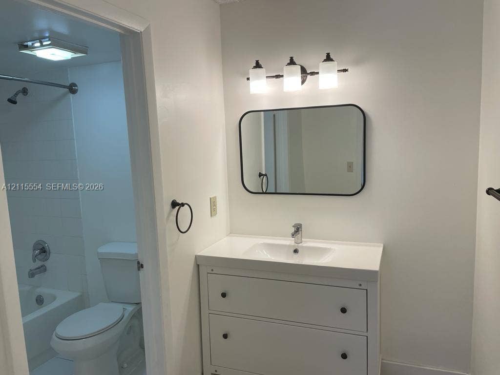 10781 Cleary Boulevard, #210, Plantation, Plantation, FL 33324 Bathroom featuring a vanity with a rectangular sink, a rounded rectangular wall mirror with a black frame, a three-light fixture with frosted glass shades, and a shower-tub combination
