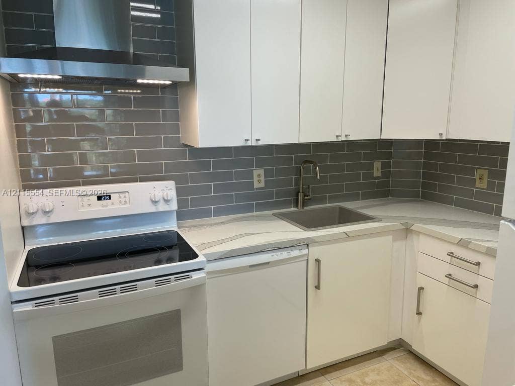 10781 Cleary Boulevard, #210, Plantation, Plantation, FL 33324 Kitchen featuring white cabinetry, solid-surface countertops with grey veining, subway tile backsplash, stainless steel range hood, and integrated sink with gooseneck faucet