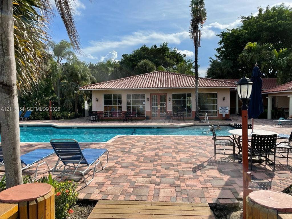 10781 Cleary Boulevard, #210, Plantation, Plantation, FL 33324 Outdoor swimming pool featuring a multi-tone paver deck, terracotta-style roof tiles, and extensive grid-pane windows