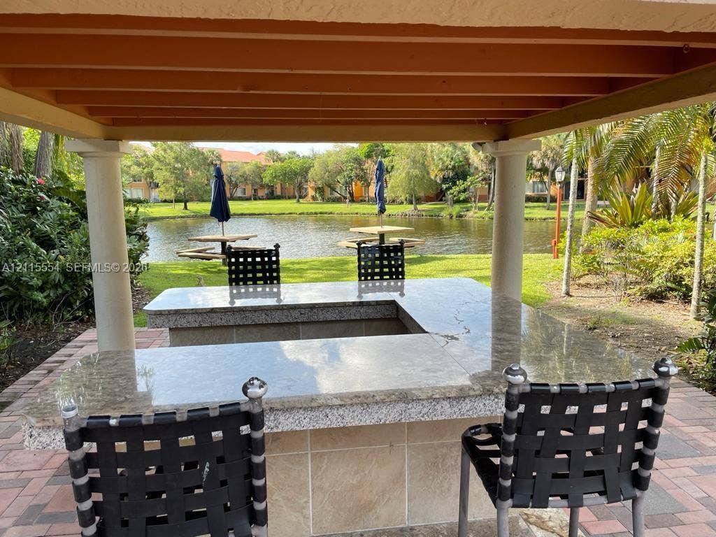 10781 Cleary Boulevard, #210, Plantation, Plantation, FL 33324 Outdoor kitchen area featuring a U-shaped stone countertop, structural pergola, and paver flooring