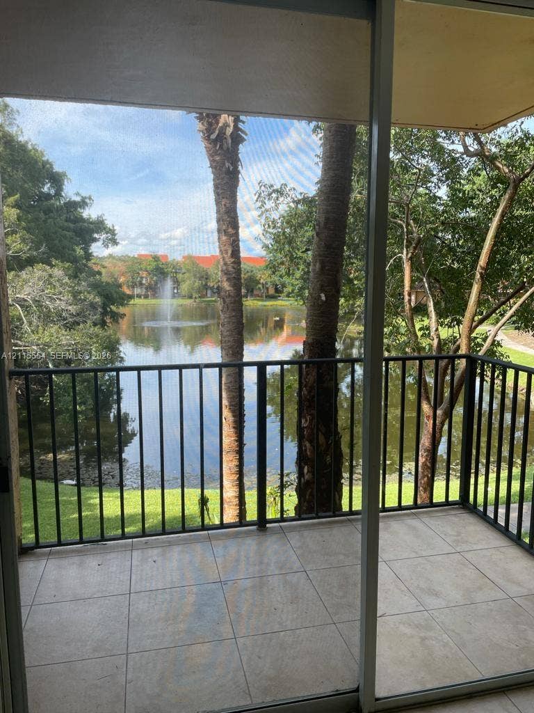 10781 Cleary Boulevard, #210, Plantation, Plantation, FL 33324 Screened balcony featuring large-format tile flooring and metal railings, overlooking a lake with a central fountain