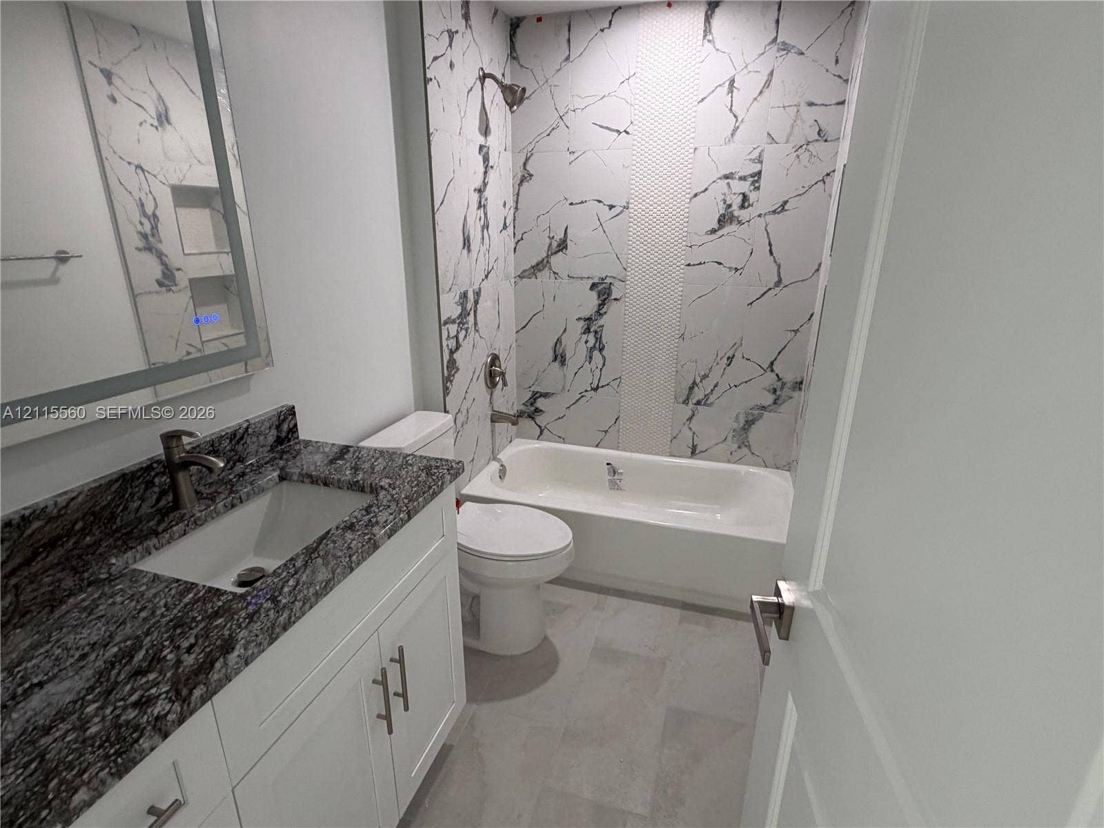 105 Concord Loop, Labelle, FL 33935 Bathroom featuring a vanity with stone-finish countertop, under-mount sink, white cabinetry with brushed metal hardware, and a bathtub surround with patterned wall tile and an integrated recessed niche