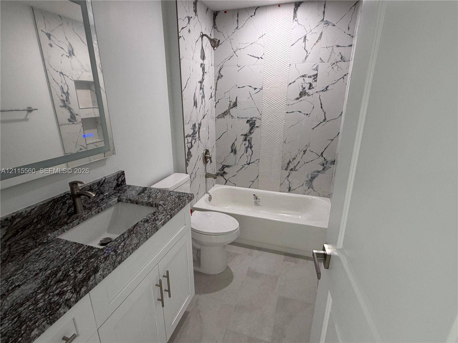 105 Concord Loop, Labelle, FL 33935 Bathroom featuring a vanity with stone-finish countertop, undermount sink, porcelain tile tub surround with an integrated shower niche, and rectangular floor tiling