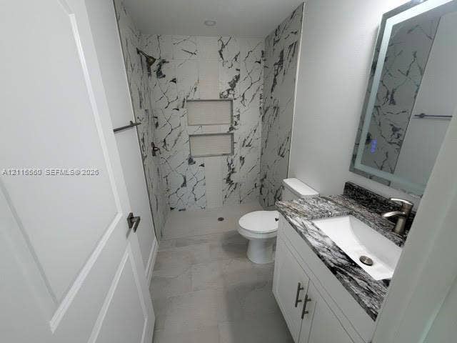 105 Concord Loop, Labelle, FL 33935 Bathroom featuring a walk-in shower with stone-patterned tile, dual built-in shower niches, vanity with a stone countertop and integrated sink, and an LED-backlit mirror