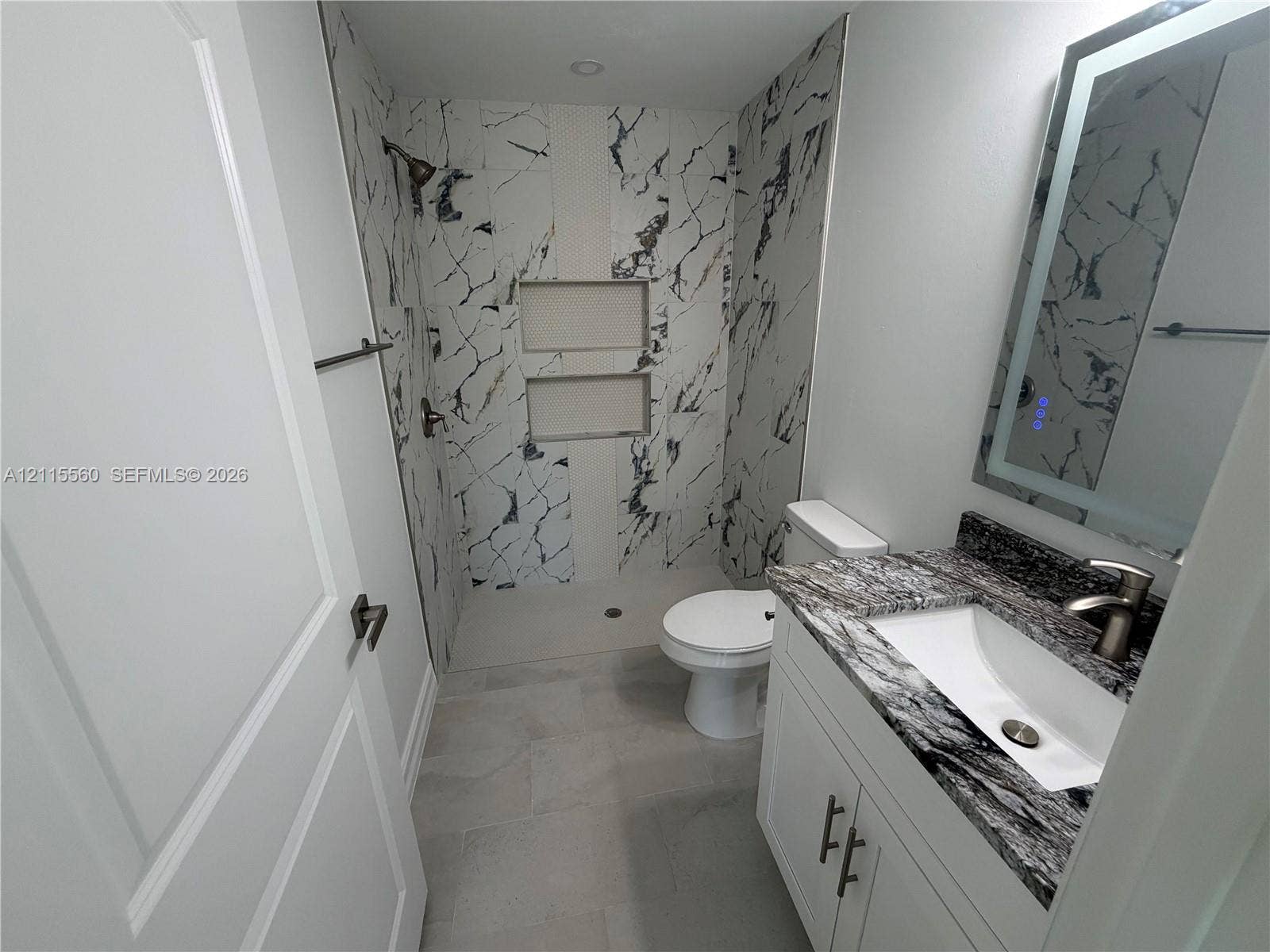 105 Concord Loop, Labelle, FL 33935 Bathroom featuring a shower with dual built-in niches, stone-patterned tile surround, vanity with a decorative stone countertop, undermount sink, and integrated LED-lit mirror
