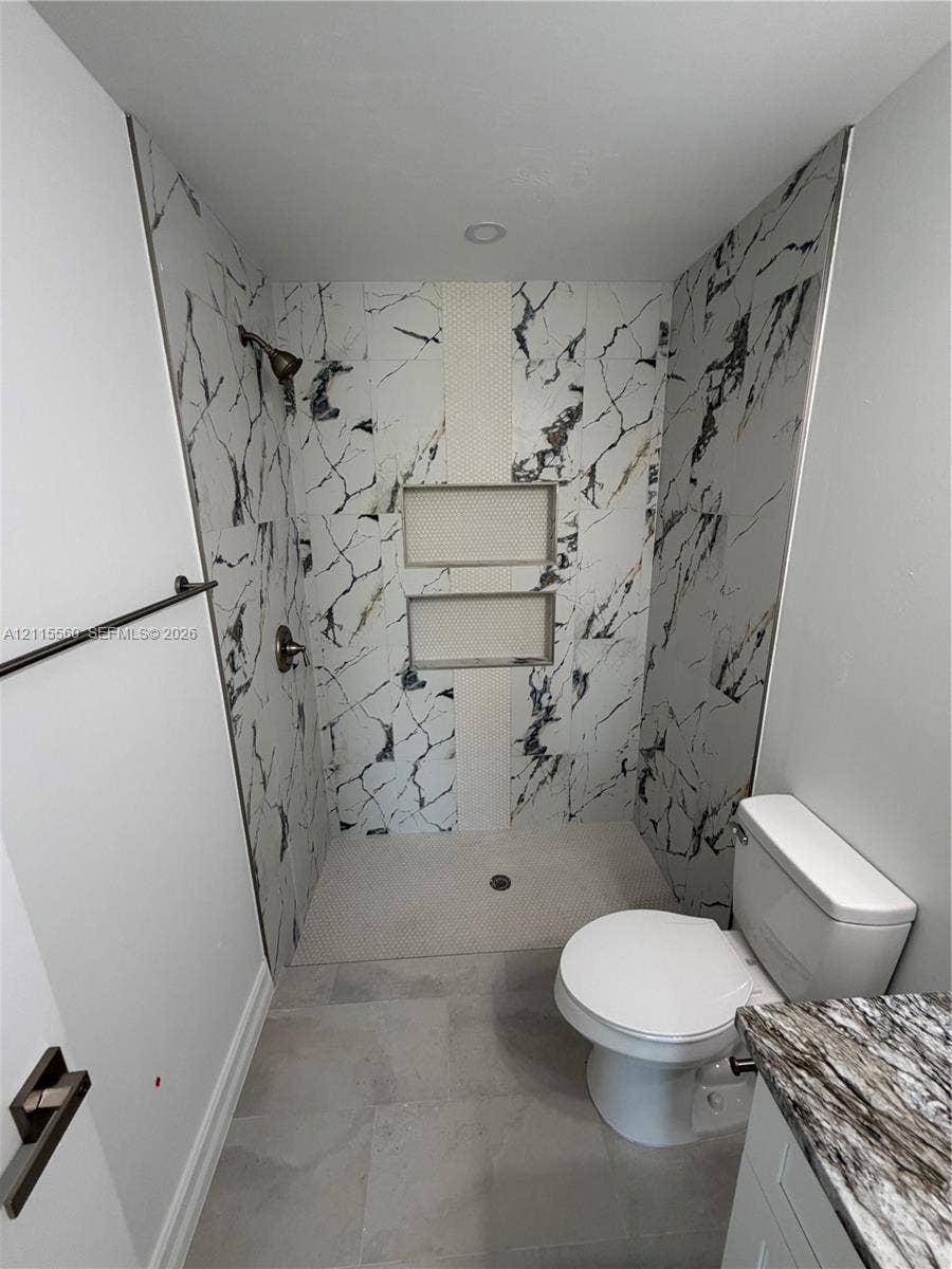 105 Concord Loop, Labelle, FL 33935 Walk-in shower featuring large-format patterned wall tile, dual recessed shelving niches, a textured stone-tiled floor, and a metal shower fixture