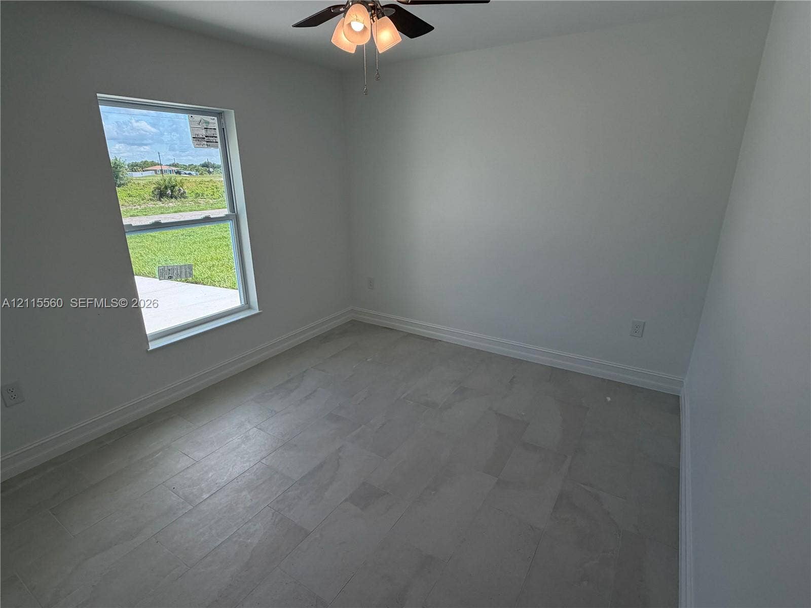 105 Concord Loop, Labelle, FL 33935 Interior space featuring neutral-toned tile flooring, light-colored wall finishes, a single-hung window, and an attached ceiling fan with multi-light fixture
