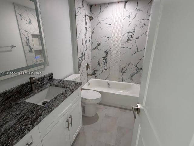 105 Concord Loop, Labelle, FL 33935 Bathroom featuring a white vanity with stone-finish countertop, undermount sink, illuminated mirror, and a tub-shower combination with floor-to-ceiling patterned wall tile