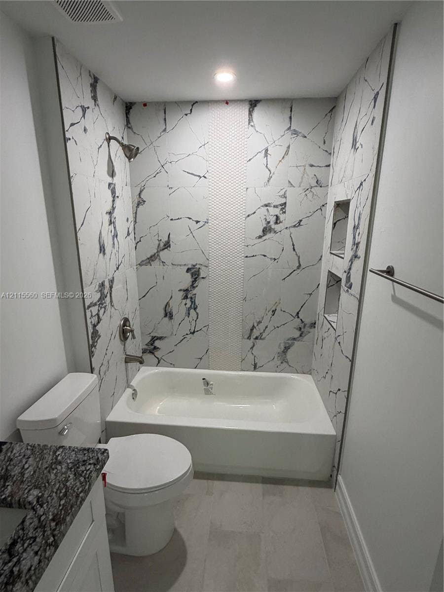 105 Concord Loop, Labelle, FL 33935 Bathroom featuring white and grey large-format stone-look wall tiles with a central mosaic vertical accent, built-in dual recessed shower shelving, a white acrylic tub, and a vanity with a dark-patterned stone-look countertop
