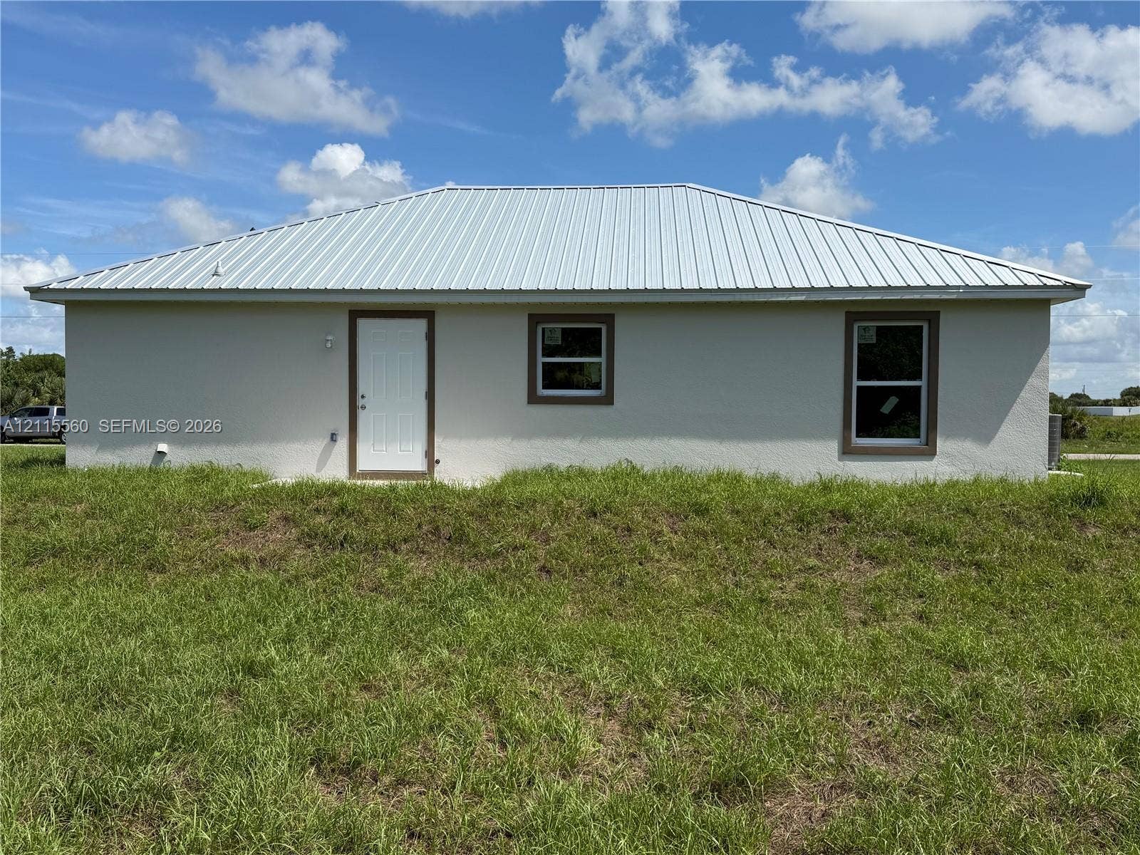 105 Concord Loop, Labelle, FL 33935 Stucco exterior featuring a metal roof, white entry door, and rectangular windows with trim