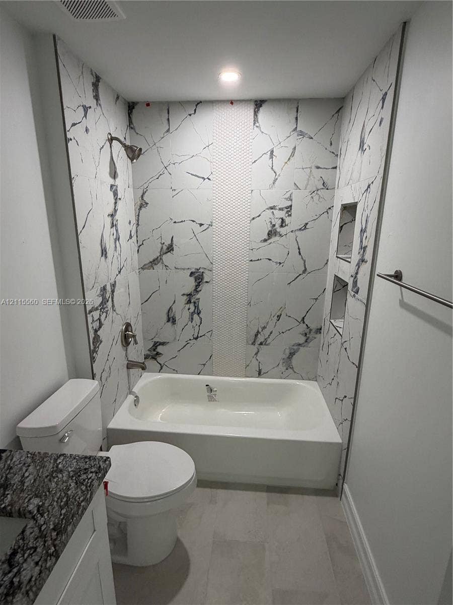 105 Concord Loop, Labelle, FL 33935 Full-height tub surround with large-format veined tile, vertical mosaic accent inlay, built-in double shower niches, recessed ceiling lighting, and stone-top vanity
