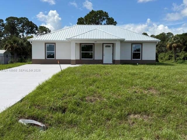 105 Concord Loop, Labelle, FL 33935 Single-story residence featuring a light-colored stucco exterior, a metal roof, dark trim accents, and a concrete driveway