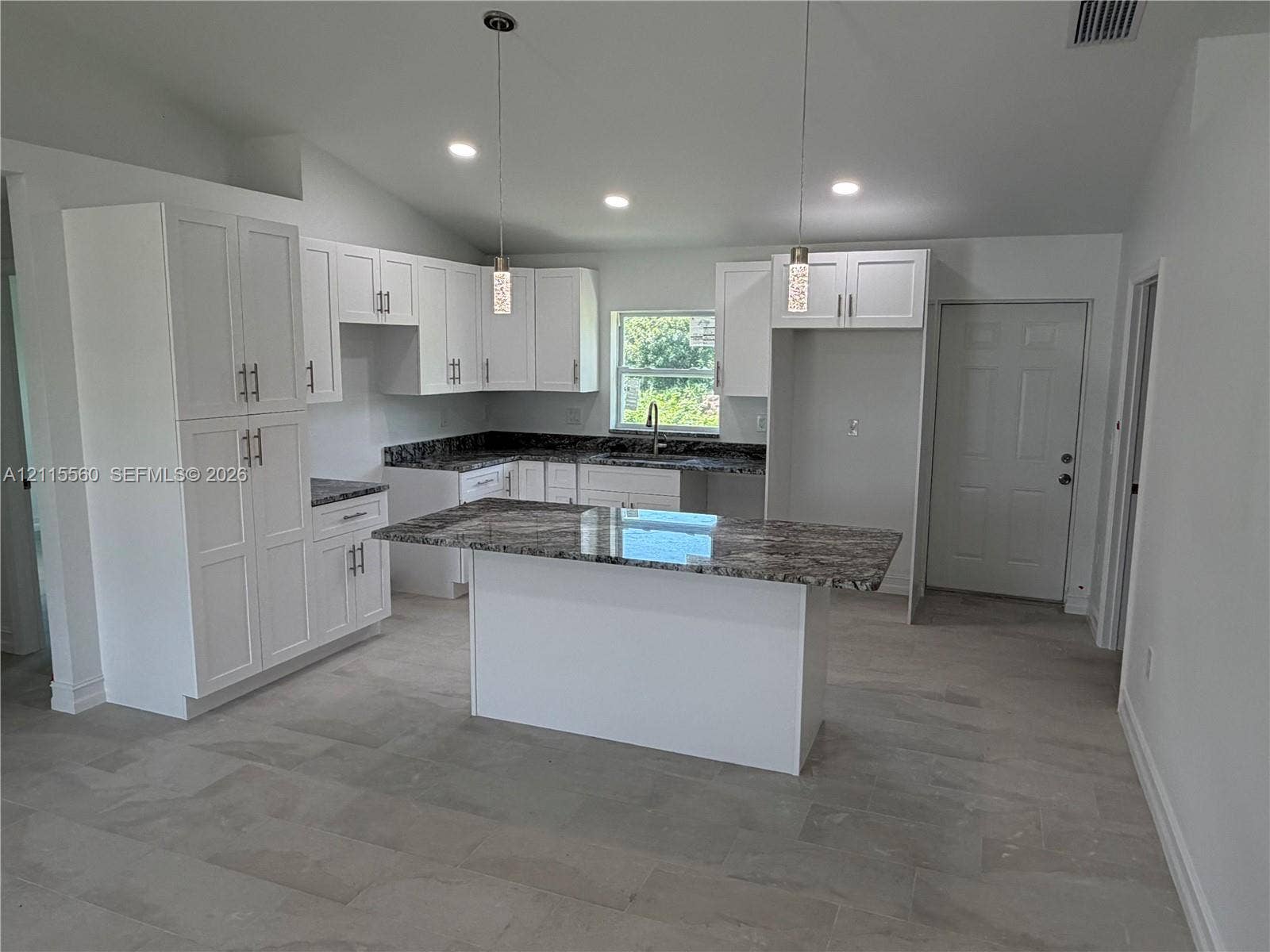 105 Concord Loop, Labelle, FL 33935 Kitchen featuring white shaker-style cabinetry, a central island with patterned stone-finish countertops, tile flooring, and dual hanging pendant lights