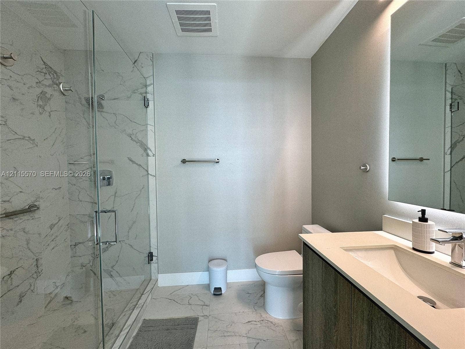 17550 Collins Avenue, #1401, Sunny Isles Beach, Sunny Isles Beach, FL 33160 Walk-in shower with floor-to-ceiling stone-look tile, frameless glass enclosure, wood-finish vanity with a quartz countertop, and a backlit wall mirror