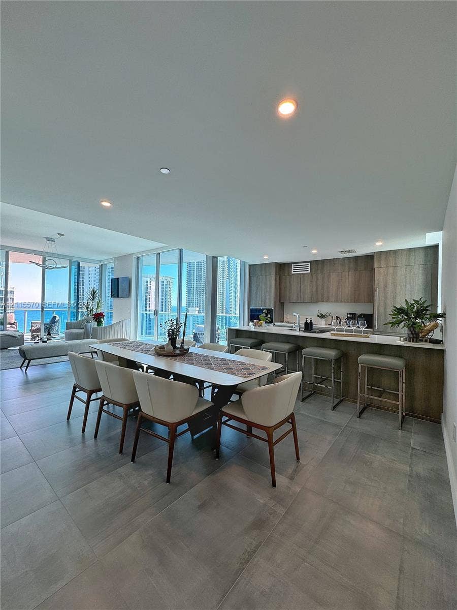 17550 Collins Avenue, #1401, Sunny Isles Beach, Sunny Isles Beach, FL 33160 Open-concept interior featuring large-format tile flooring, flat-panel cabinetry, a kitchen island with bar seating, and expansive floor-to-ceiling glass windows