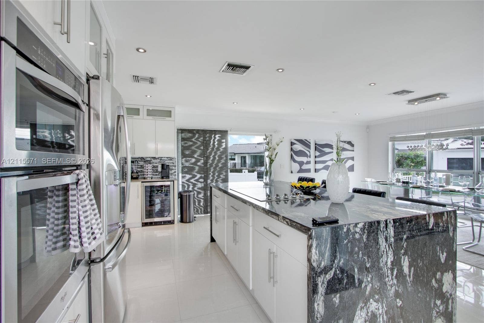 2001 NE 122nd Road, North Miami, FL 33181 Kitchen featuring a center island with stone surfacing, stainless steel double wall ovens, stainless steel refrigerator, white cabinetry, and built-in under-counter beverage storage